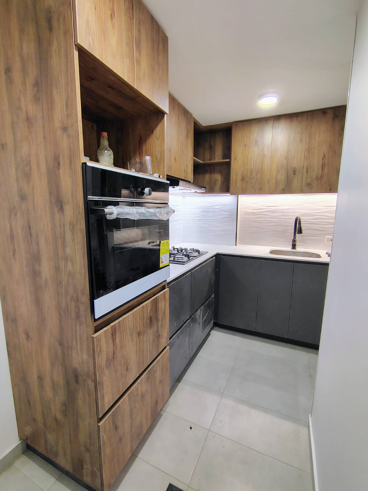 Cocina integral en madera y gris con torre de horno y mesón en cuarzo