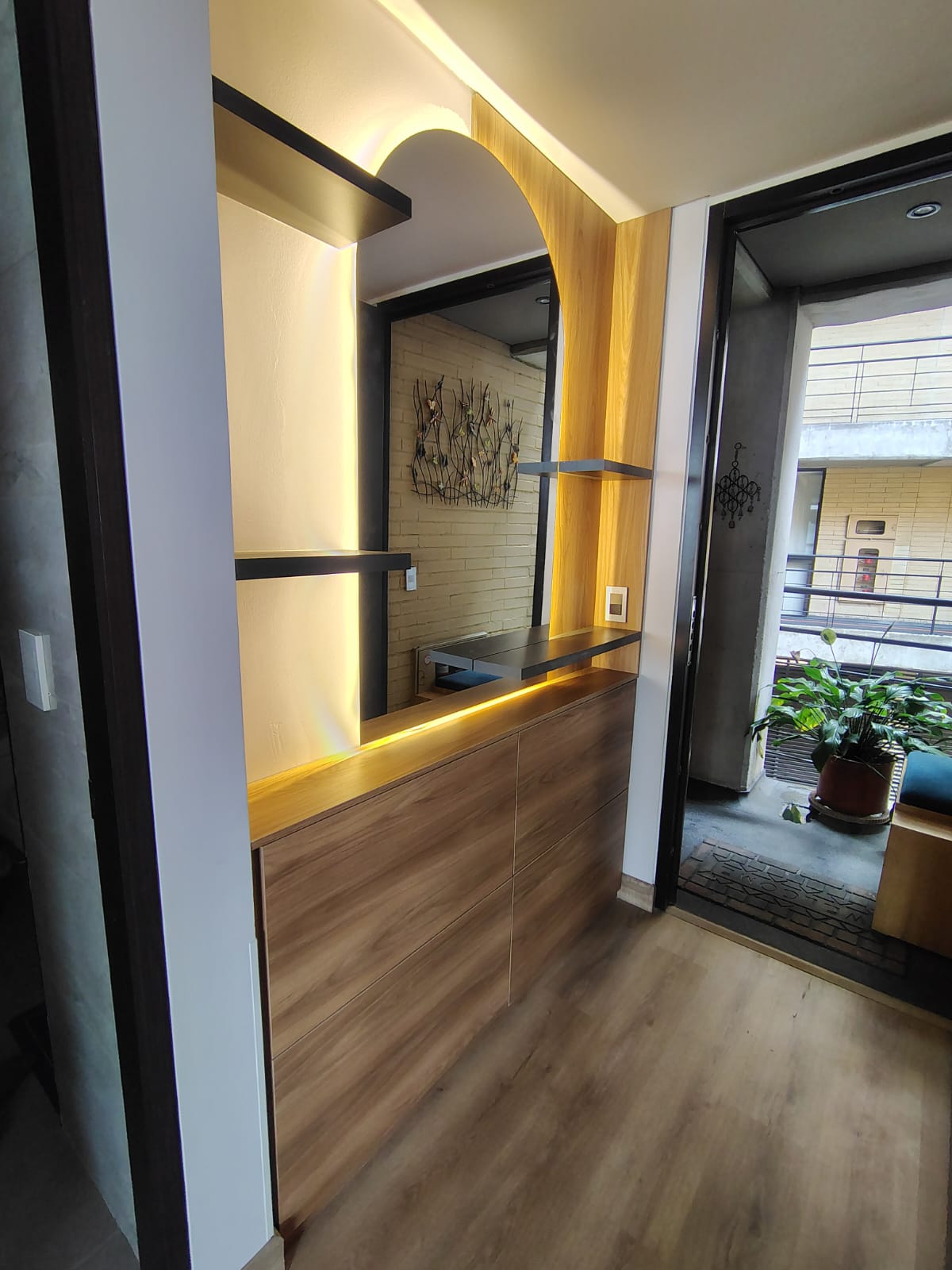 Recibidor a medida con arco iluminado, repisas negras y mueble en madera