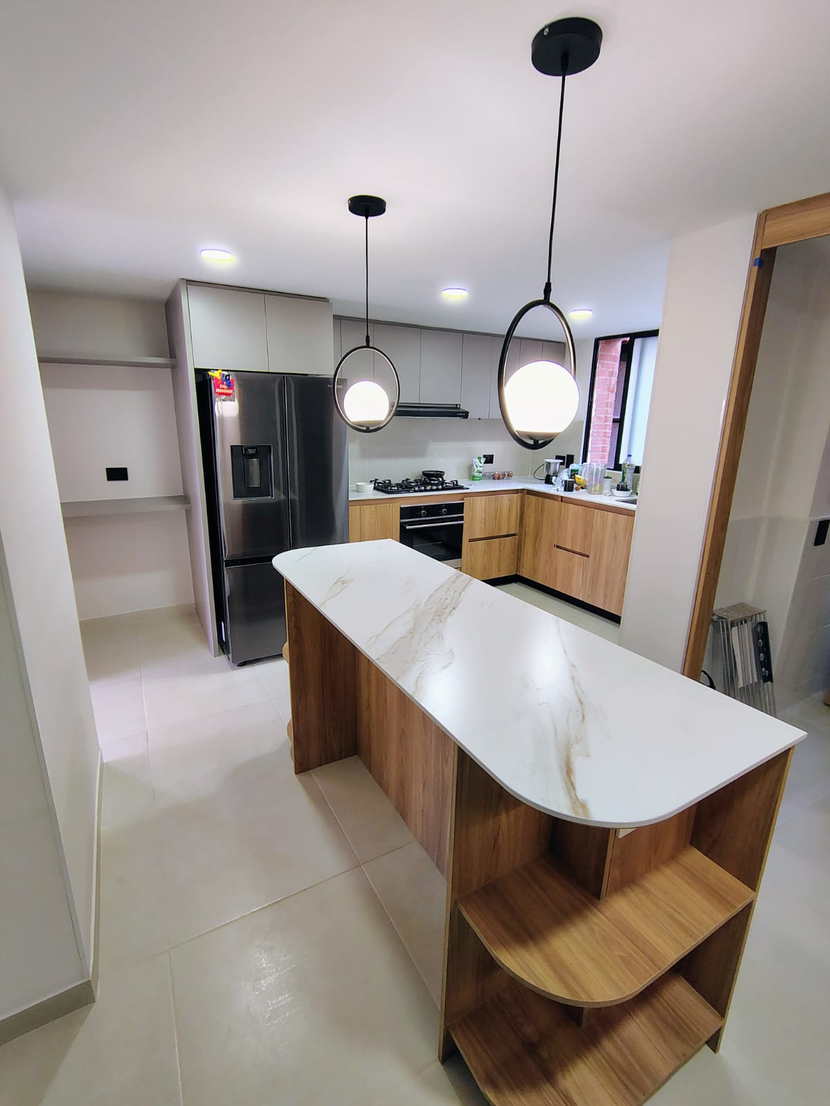 Cocina integral con isla en mesón tipo mármol, madera natural y repisas curvas