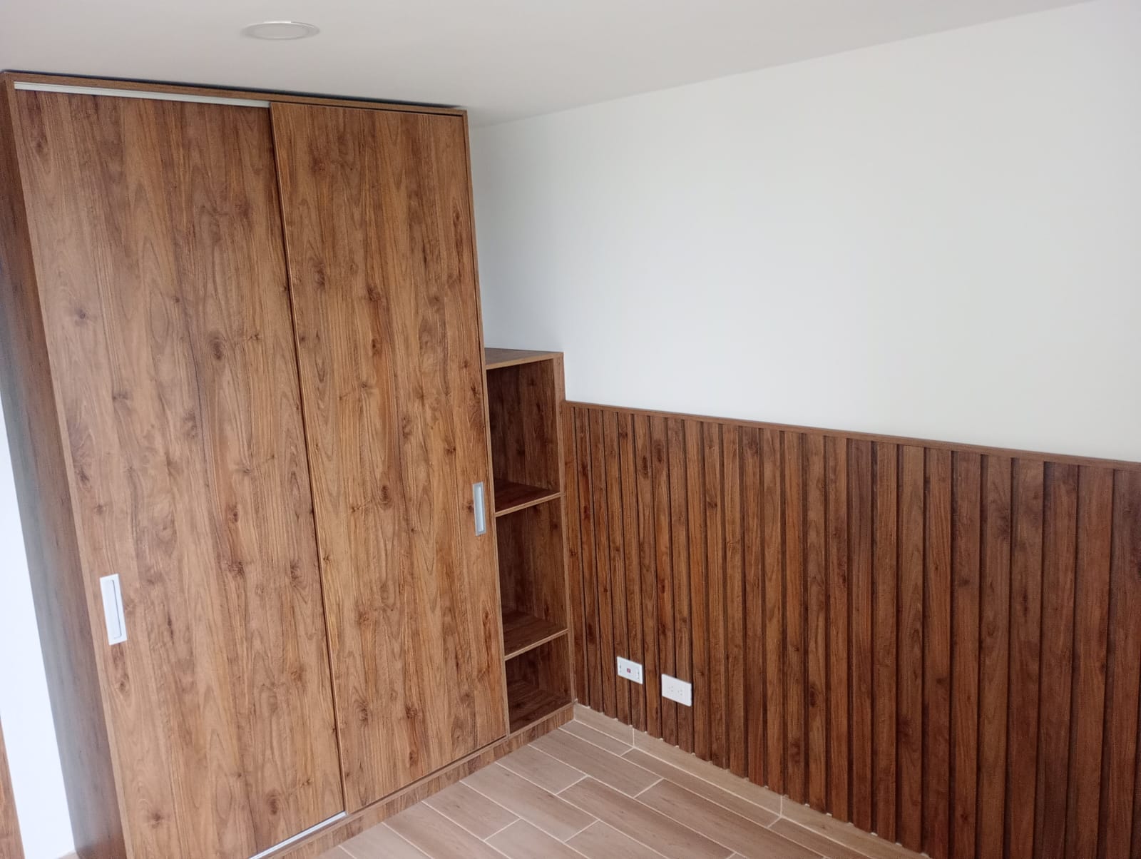 Clóset corredizo en madera con nicho de repisas y panel de listones en la pared