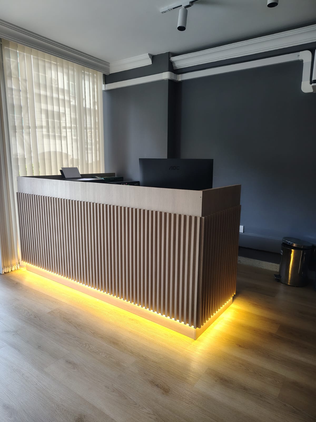 Recepción a medida en madera con listones verticales e iluminación LED