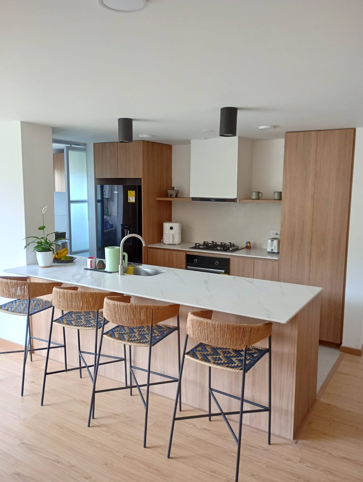 Cocina integral en madera clara con península, mesón tipo mármol y barra para comedor
