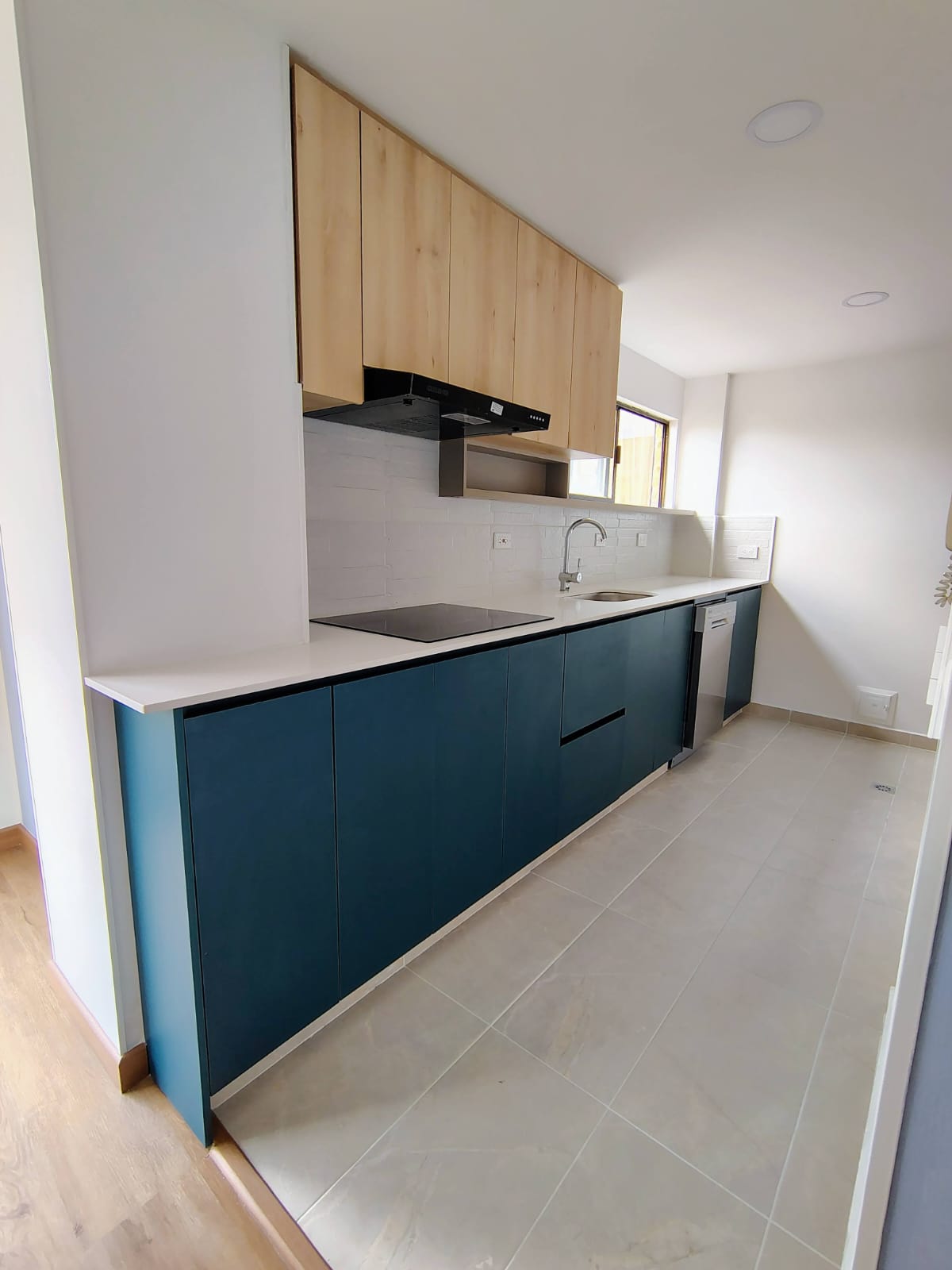 Cocina integral lineal azul petróleo con muebles altos en madera y mesón blanco
